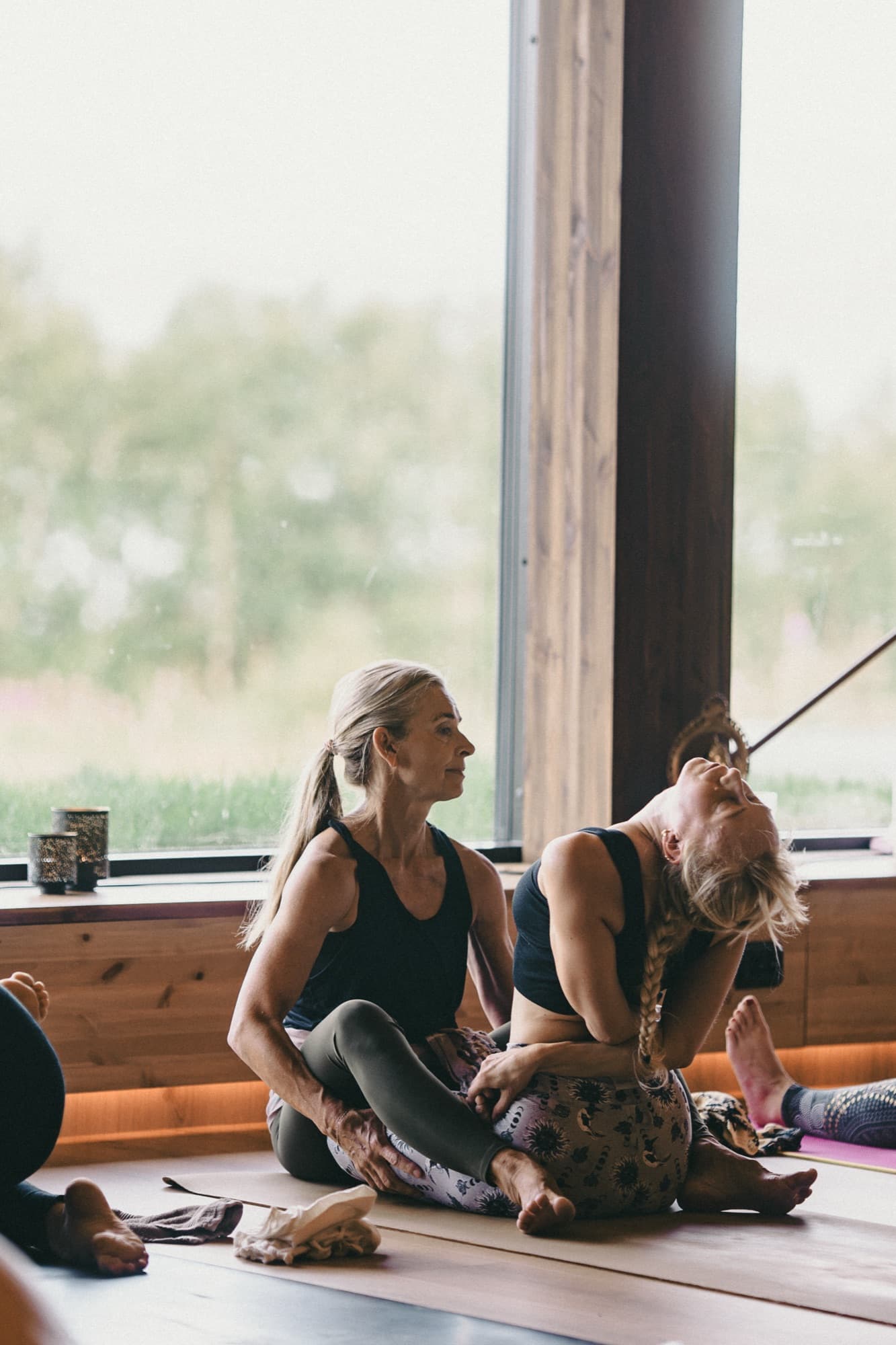 Lotta assisting a student in a seated backbend by the window