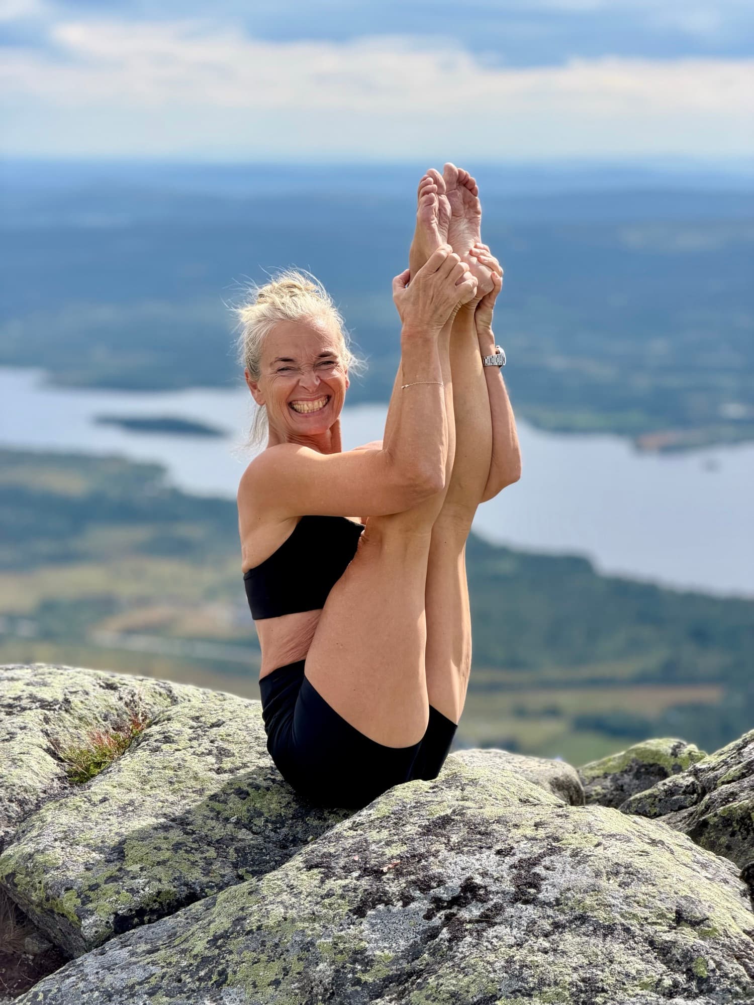 Lotta laughing in a seated balance on a mountaintop above a lake