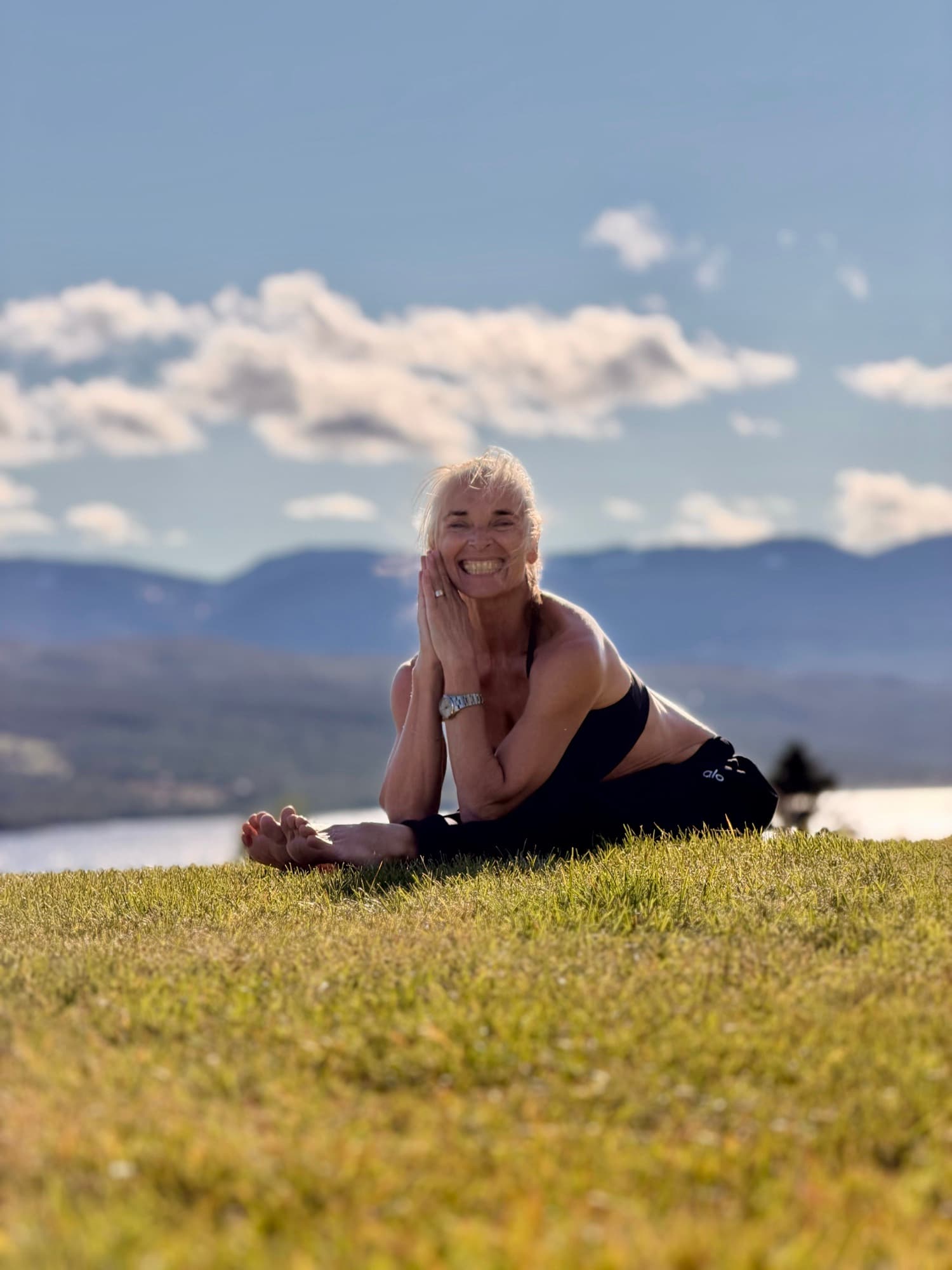 Lotta smiling on a grassy hill above a lake, hands together